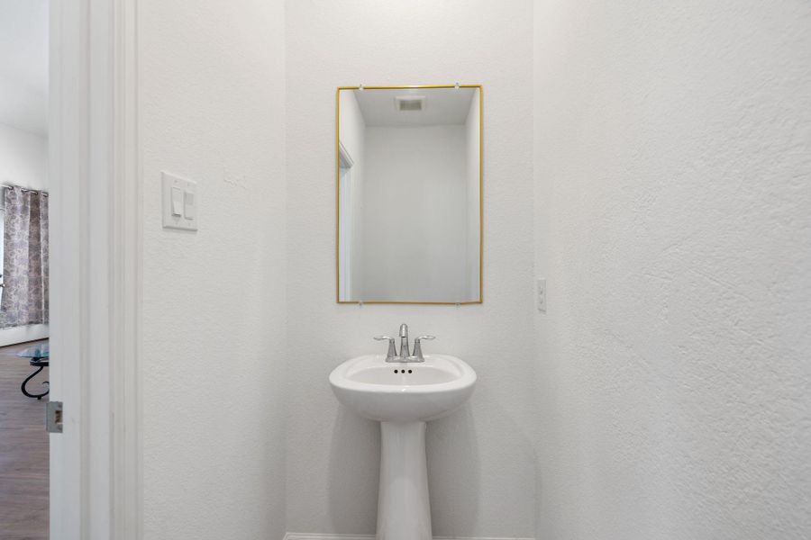 Downstairs powder room has a simple and beautiful pedestal sink with gold frame mirror.
