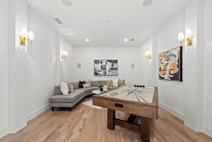 This versatile room features light-toned hardwood flooring and recessed lighting, complemented by wall sconces