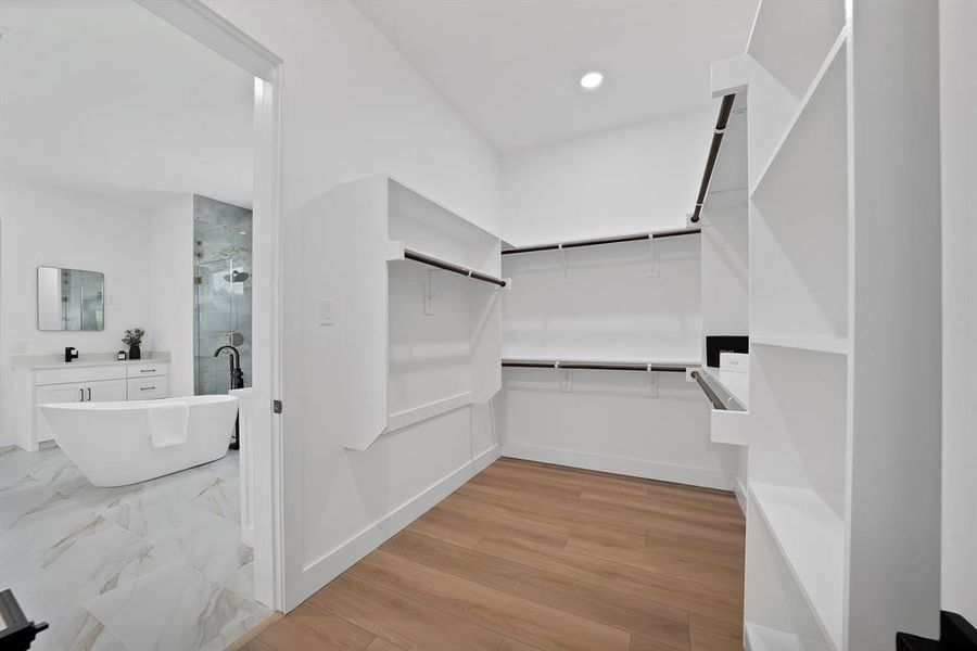 Walk-in closet with wood-finish flooring, extensive built-in shelving, and multiple hanging rods