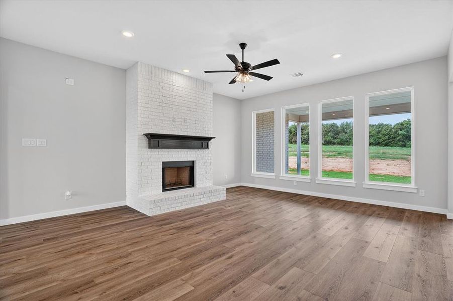 Spacious room featuring a white brick fireplace with a dark wood mantel, wood-finish flooring, recessed lighting, and a ceiling fan