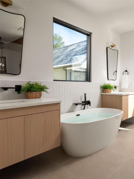 Full bath featuring two vanities, dark tile patterned floors, a freestanding bath, and tile walls