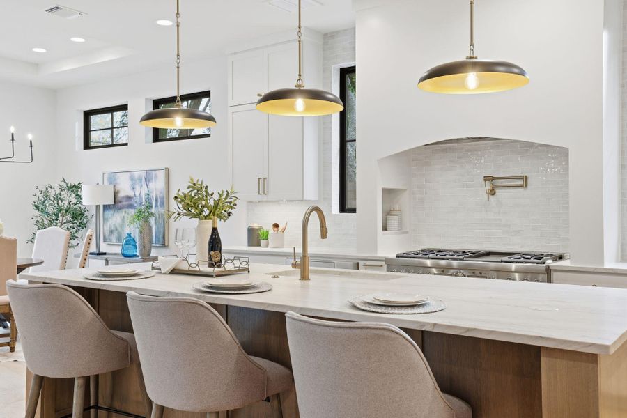 Kitchen featuring a kitchen bar, light stone counters, pendant lighting, backsplash, and white cabinetry