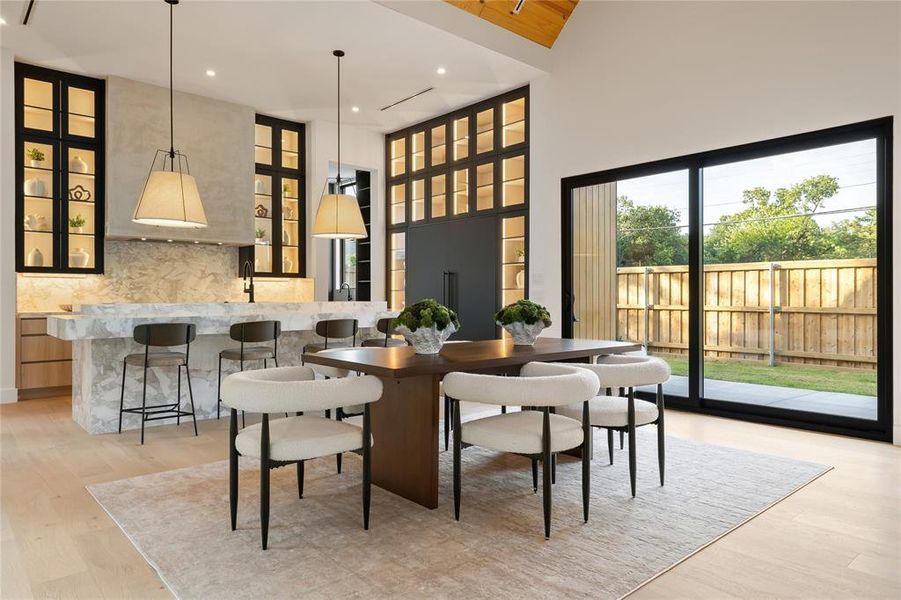 Open-concept living area featuring light wood-finish flooring, a large kitchen island with integrated seating, and a dining space Open-concept living area featuring light wood-finish flooring, a large kitchen island with integrated seating, and a dining space