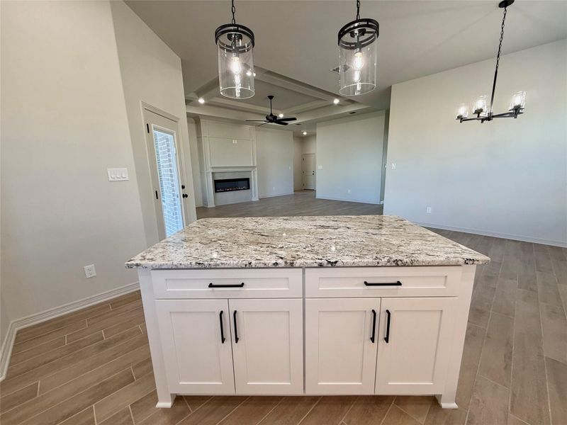 Kitchen featuring a glass covered fireplace, wood tiled floors, a kitchen island, hanging light fixtures, and a ceiling fan