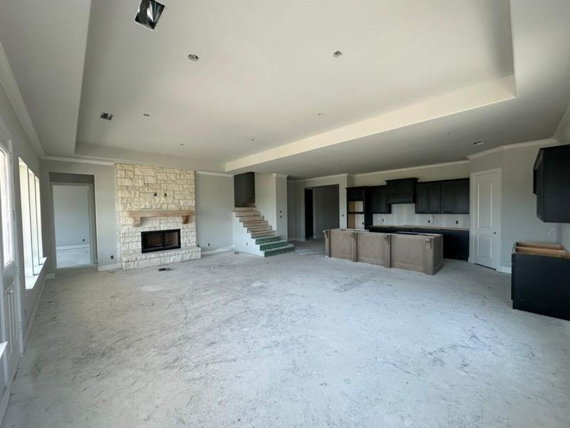 Expansive living space featuring a stone fireplace with a substantial mantel, tray ceilings, and recessed lighting