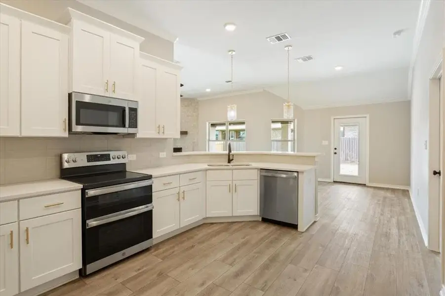 Kitchen featuring appliances with stainless steel finishes, plenty of natural light, a peninsula, ornamental molding, and decorative backsplash Kitchen featuring appliances with stainless steel finishes, plenty of natural light, a peninsula, ornamental molding, and decorative backsplash