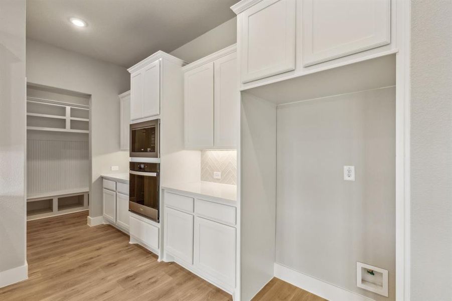 Kitchen with white cabinetry, stainless steel oven, backsplash, and built in microwave