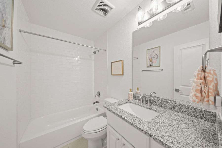 This ensuite bath features tile floors, a granite counter and a tub/shower combo with subway tile extending to the ceiling.
