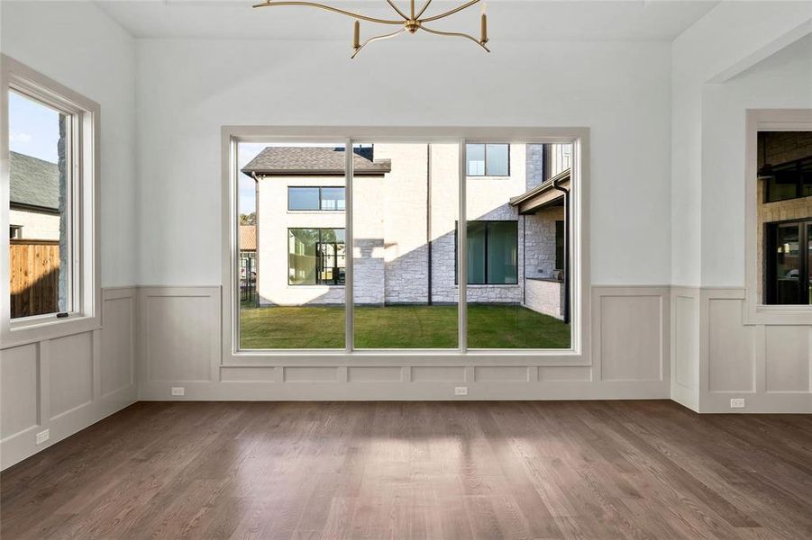 Unfurnished dining area with wainscoting, wood finished floors, plenty of natural light, a decorative wall, and a chandelier Unfurnished dining area with wainscoting, wood finished floors, plenty of natural light, a decorative wall, and a chandelier