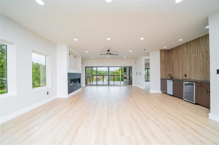 Unfurnished living room featuring beverage cooler, a fireplace, bar, light wood-type flooring, and recessed lighting Unfurnished living room featuring beverage cooler, a fireplace, bar, light wood-type flooring, and recessed lighting