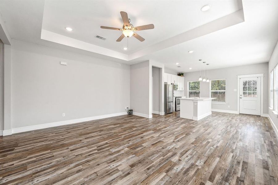 Unfurnished living room featuring a tray ceiling, recessed lighting, light wood-style flooring, and ceiling fan Unfurnished living room featuring a tray ceiling, recessed lighting, light wood-style flooring, and ceiling fan