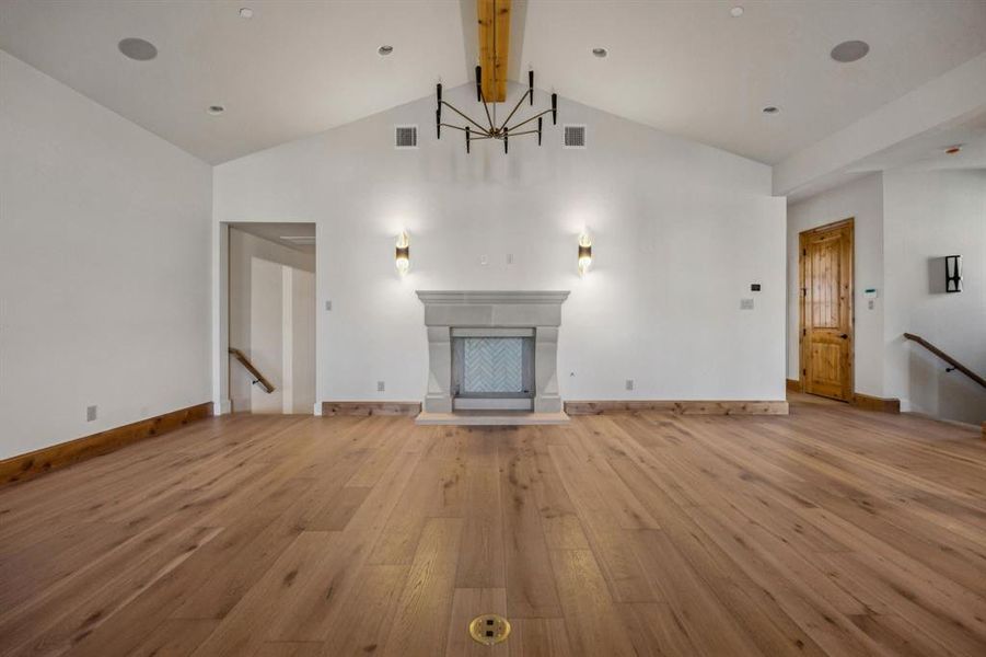 Unfurnished living room with beam ceiling, light wood-type flooring, high vaulted ceiling, a fireplace, and a chandelier