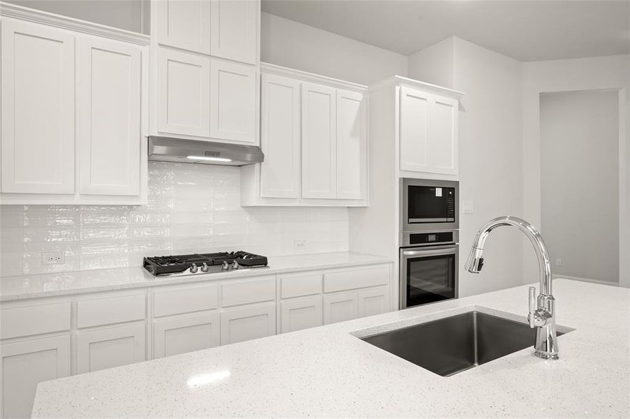 Kitchen featuring under cabinet range hood, stainless steel appliances, a sink, white cabinets, and light stone countertops Kitchen featuring under cabinet range hood, stainless steel appliances, a sink, white cabinets, and light stone countertops