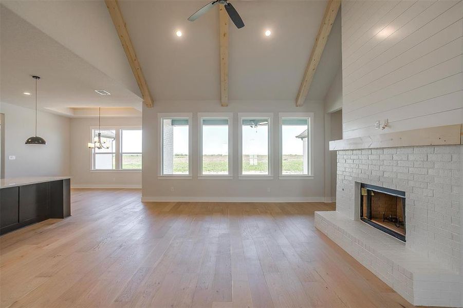 Unfurnished living room featuring ceiling fan with notable chandelier, beamed ceiling, a fireplace, light wood-style flooring, and baseboards Unfurnished living room featuring ceiling fan with notable chandelier, beamed ceiling, a fireplace, light wood-style flooring, and baseboards