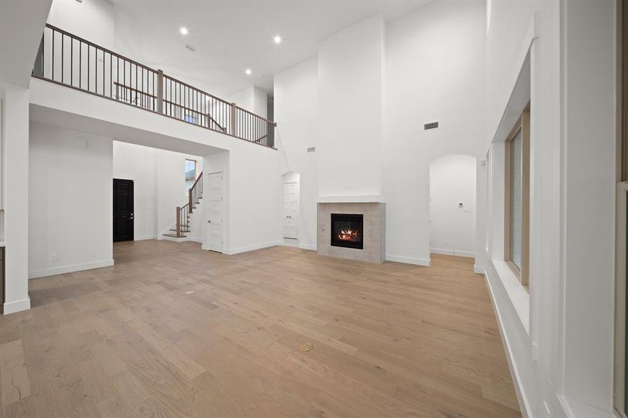 Unfurnished living room featuring a towering ceiling, a tile fireplace, light wood finished floors, stairs, and recessed lighting