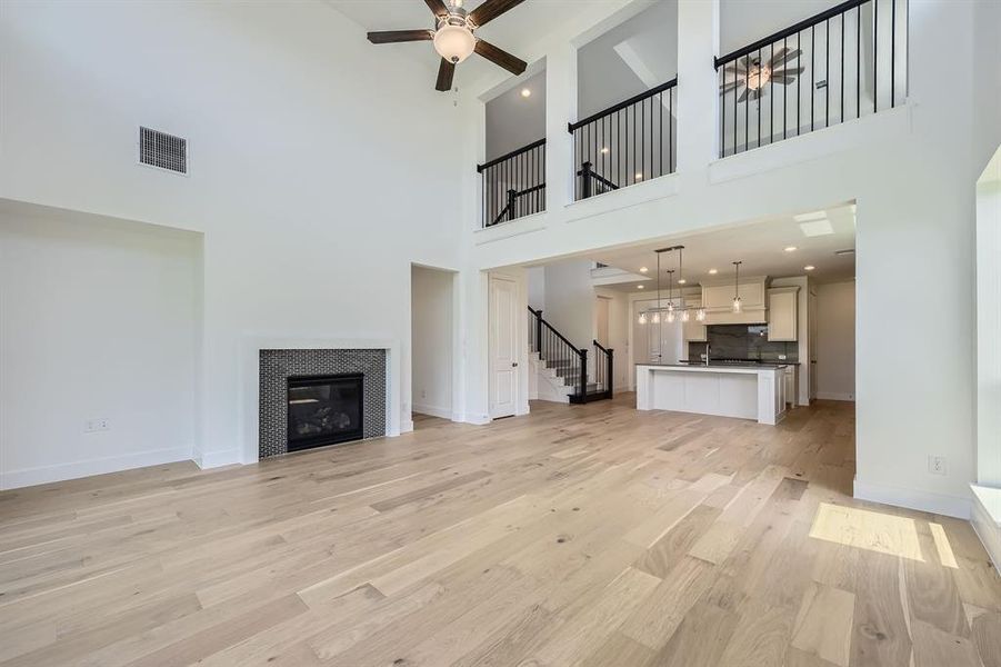 Unfurnished living room featuring stairs, light wood finished floors, ceiling fan, a towering ceiling, and baseboards Unfurnished living room featuring stairs, light wood finished floors, ceiling fan, a towering ceiling, and baseboards