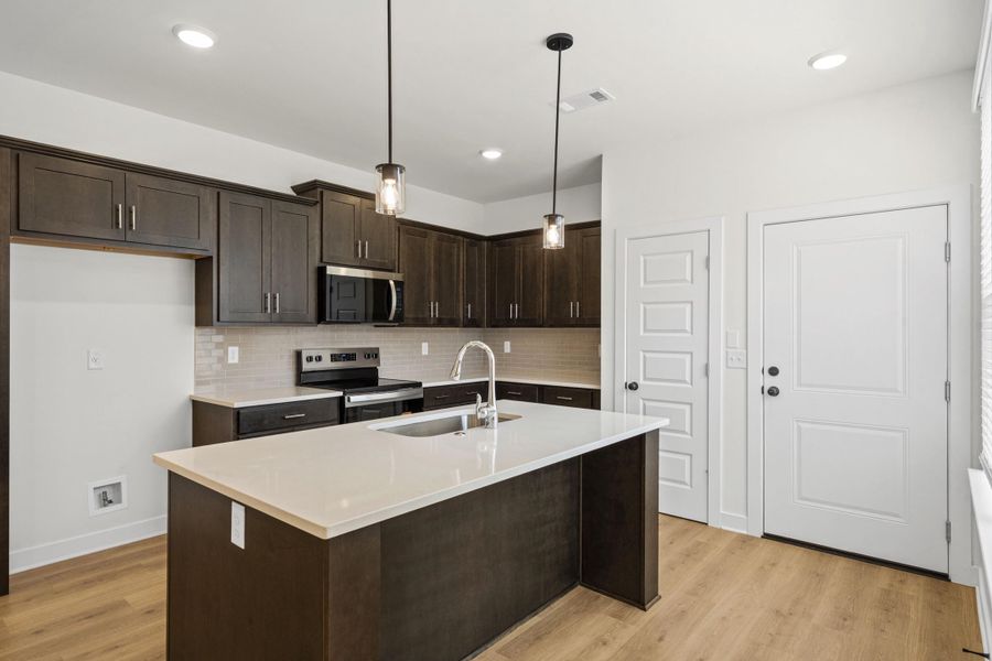 Contemporary kitchen featuring dark wood cabinetry, a light-toned countertop island with an undermount sink, and stainless steel appliances