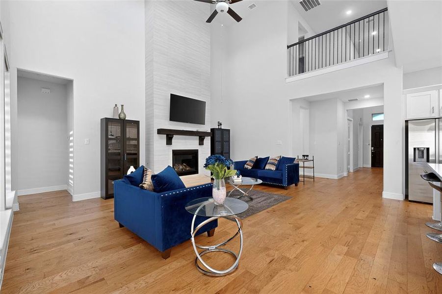 Living area featuring light wood-style floors, a fireplace, a high ceiling, and a ceiling fan