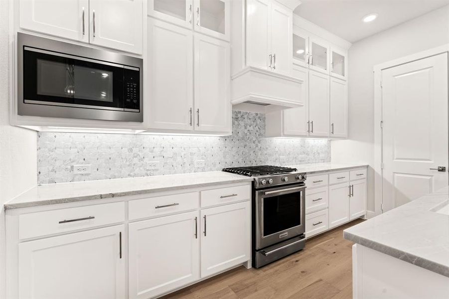 Kitchen with white cabinetry, light stone countertops, tasteful backsplash, appliances with stainless steel finishes, and light wood-type flooring