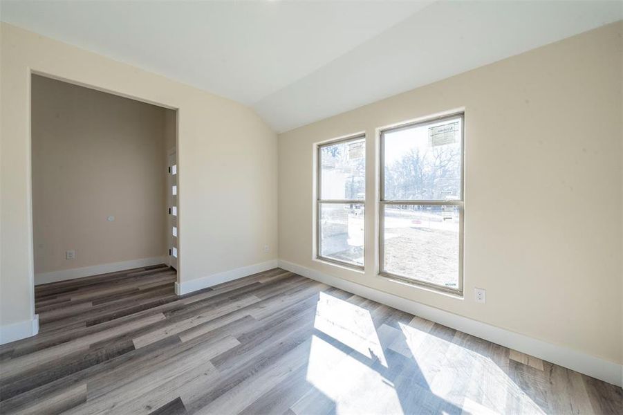 Spare room featuring lofted ceiling, baseboards, and wood finished floors