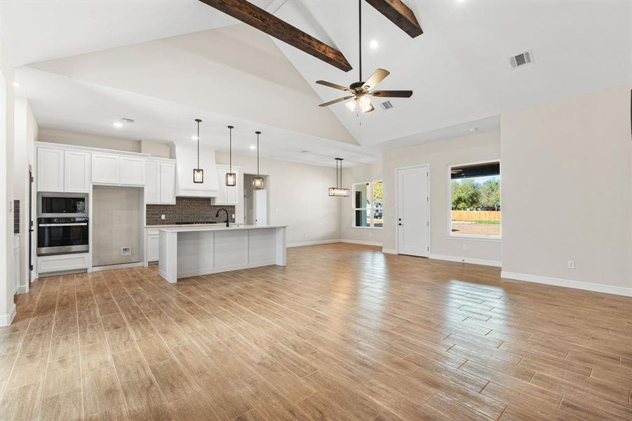Unfurnished living room featuring beam ceiling, high vaulted ceiling, light wood finished floors, a ceiling fan, and recessed lighting