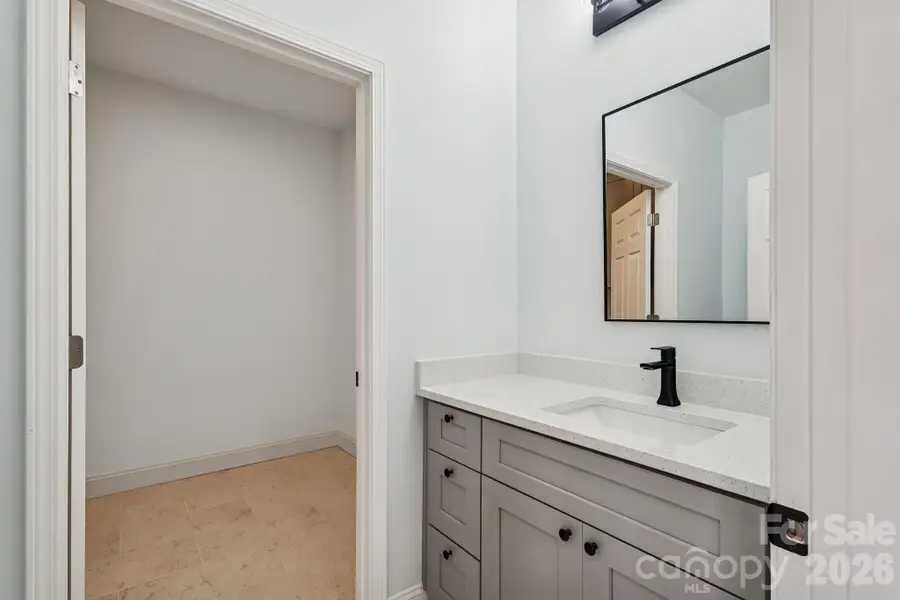 Powder room on first floor with quartz counter top, framed mirror, elegant light fixtures, tile floor and access to the laundry room