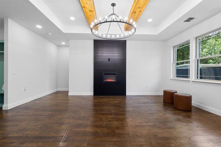 Spare room featuring a raised ceiling, a chandelier, wood finished floors, recessed lighting, and a large fireplace Spare room featuring a raised ceiling, a chandelier, wood finished floors, recessed lighting, and a large fireplace