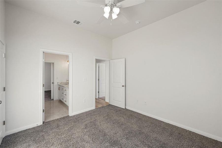 Unfurnished bedroom with light colored carpet, ensuite bath, and ceiling fan