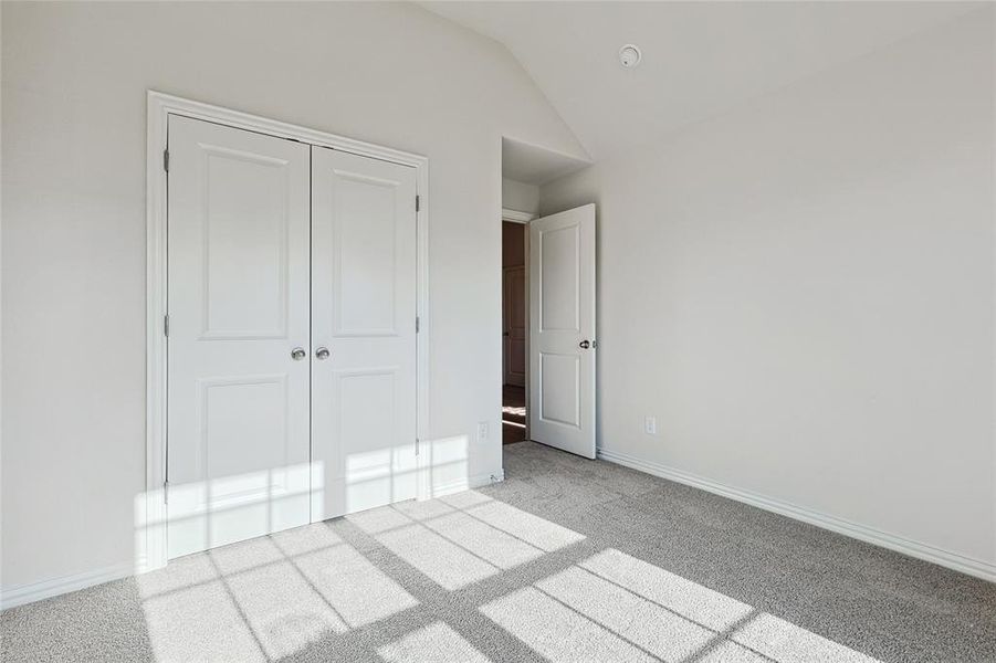 Unfurnished bedroom featuring a closet, light colored carpet, and vaulted ceiling