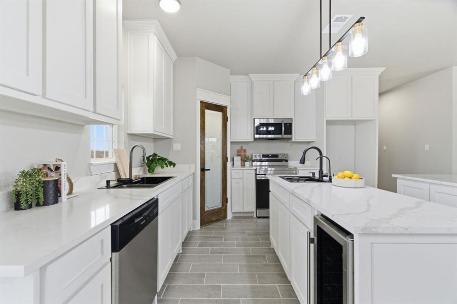 Kitchen with stainless steel appliances, beverage cooler, pendant lighting, a center island with sink, and white cabinets