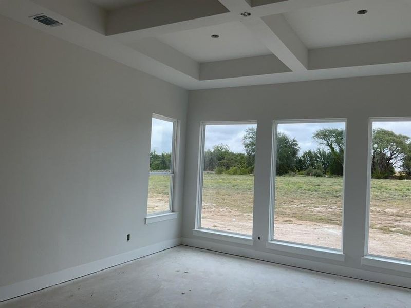 Unfurnished sunroom featuring coffered ceiling, beam ceiling, and view of wooded area