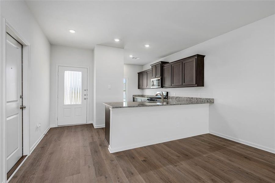 Kitchen with light stone counters, dark brown cabinetry, a peninsula, dark wood-style flooring, and appliances with stainless steel finishes