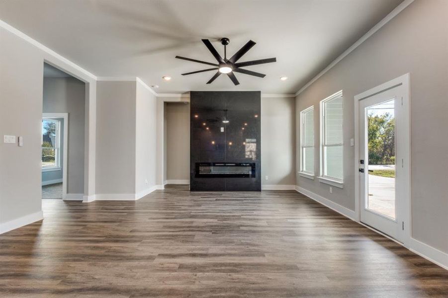 Unfurnished living room featuring a fireplace, ornamental molding, wood finished floors, and a ceiling fan