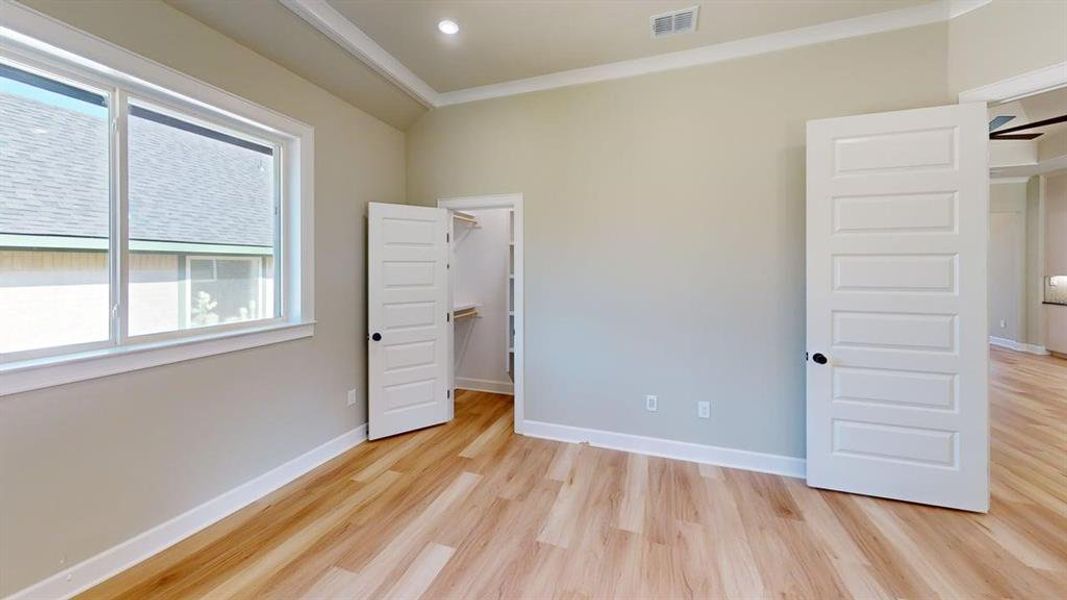 Unfurnished bedroom with multiple windows, light wood finished floors, crown molding, a spacious closet, and recessed lighting