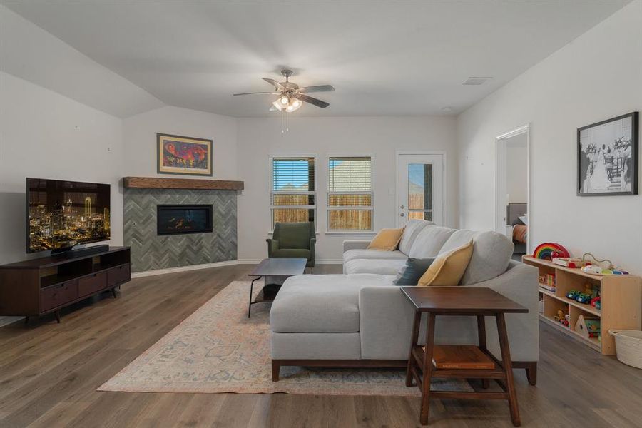 Living area featuring visible vents, a ceiling fan, a tile fireplace, wood finished floors, and vaulted ceiling