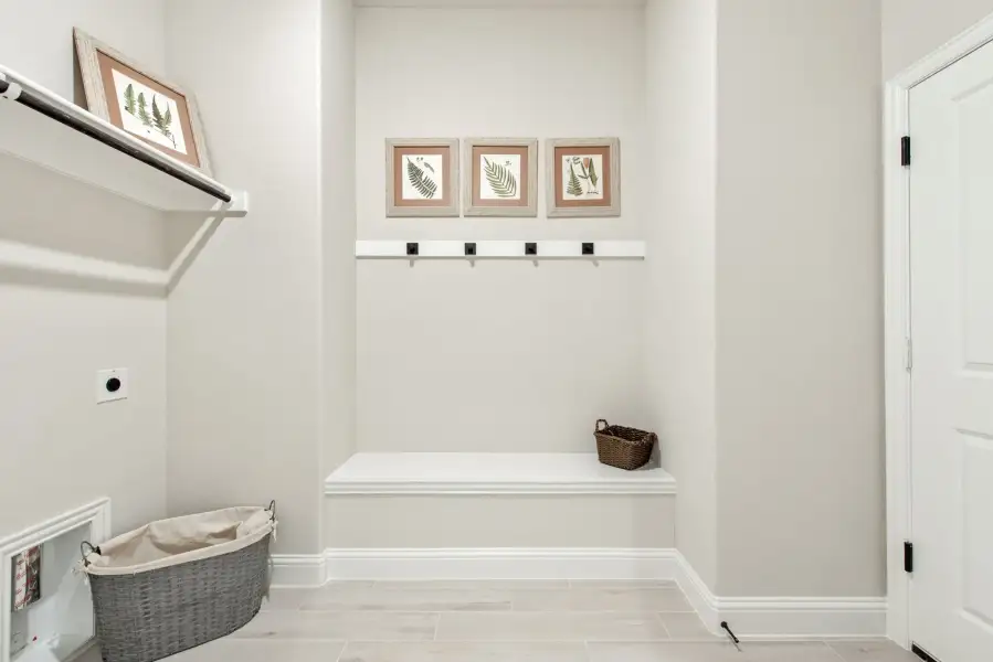 Mudroom with built-in bench, coat hooks, wall shelf, and wicker storage baskets on light tile floor