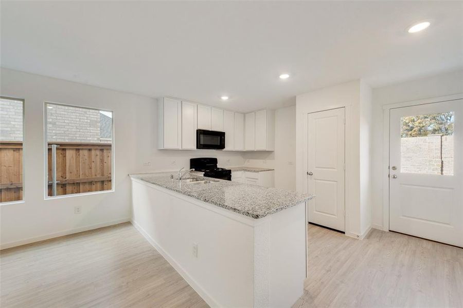 Kitchen featuring white cabinetry, light stone counters, kitchen peninsula, light hardwood / wood-style floors, and black appliances