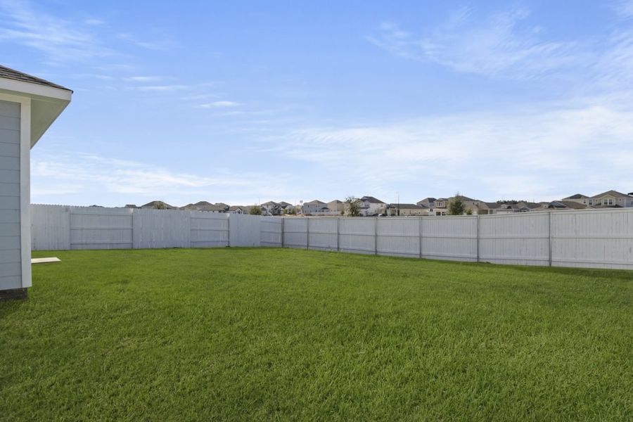 Image of a green grass backyard with a white fence and blue sky