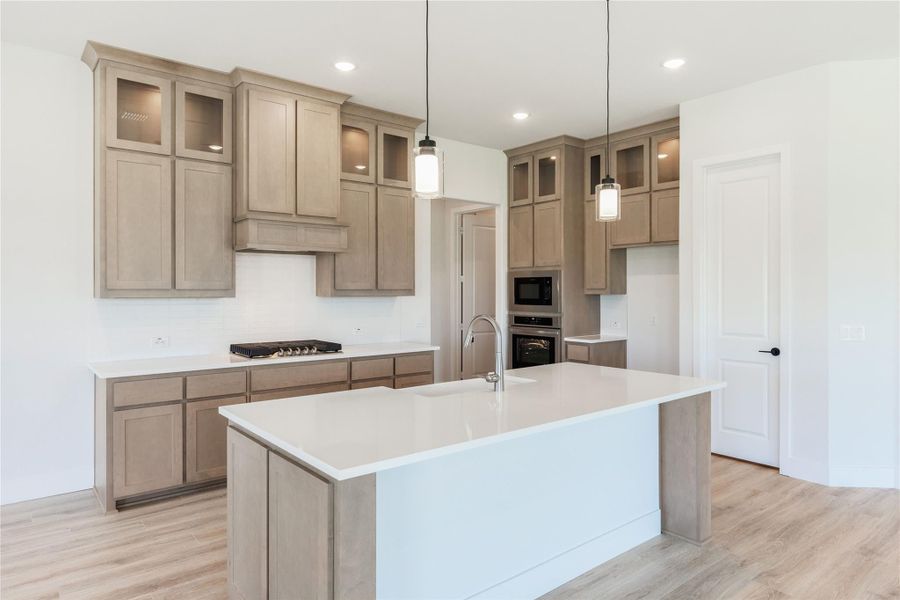 Kitchen with large center island, tan shaker cabinets, white countertops, and pendant lights over hardwood floors
