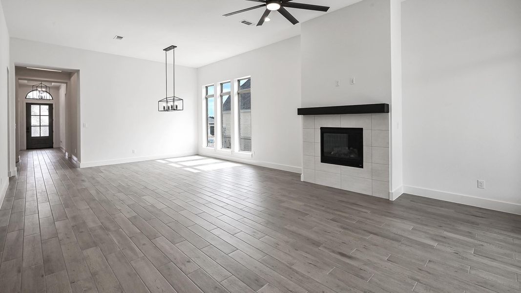 Unfurnished living room with a ceiling fan, wood finished floors, and a tiled fireplace Unfurnished living room with a ceiling fan, wood finished floors, and a tiled fireplace