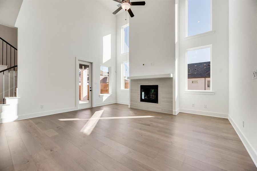 Unfurnished living room with a tile fireplace, light wood-style flooring, a ceiling fan, a high ceiling, and stairway