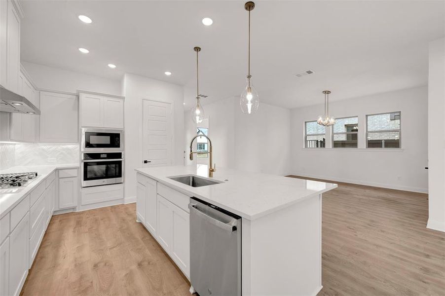 Kitchen featuring white cabinetry, stainless steel appliances, an island with sink, light wood-style floors, and light stone counters