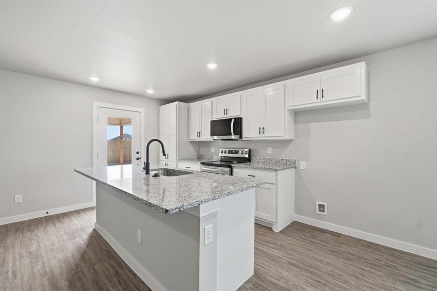 Kitchen with white cabinets, stainless steel appliances, light stone countertops, dark wood finished floors, and an island with sink