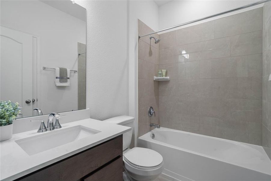 Secondary bathroom features stained cabinets, neutral paint, shower/tub combo with tile surround, large mirror, tile floors, and sleek fixtures and modern finishes.