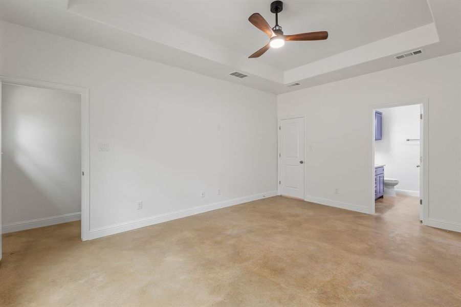 Unfurnished bedroom featuring connected bathroom, ceiling fan, and a tray ceiling