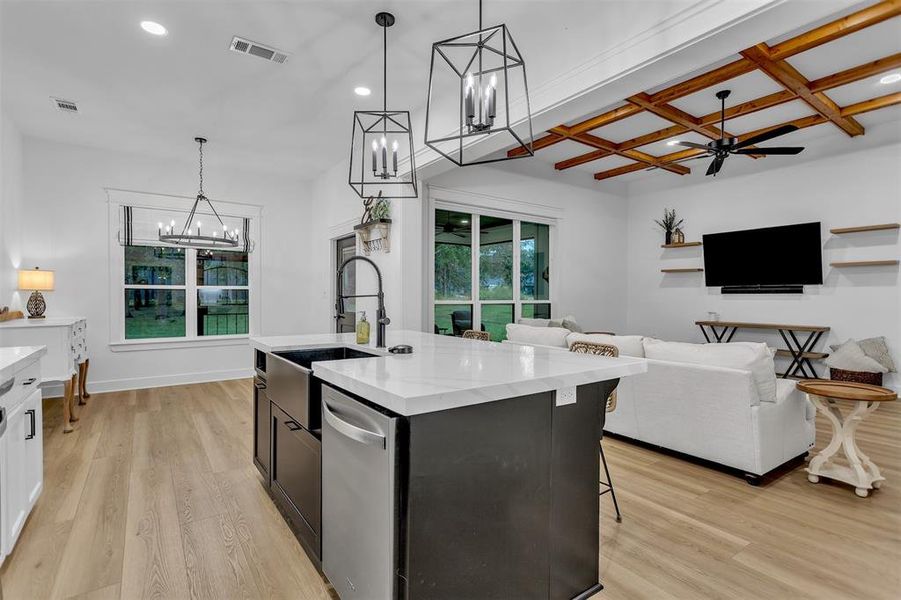Kitchen featuring decorative light fixtures, open floor plan, a kitchen island with black farmhouse sink and light stone countertops. Kitchen featuring decorative light fixtures, open floor plan, a kitchen island with black farmhouse sink and light stone countertops.