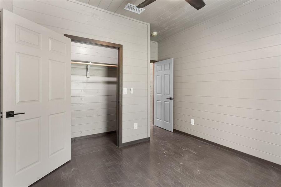 Unfurnished bedroom featuring dark wood-style flooring, baseboards, visible vents, wood walls, and wood ceiling Unfurnished bedroom featuring dark wood-style flooring, baseboards, visible vents, wood walls, and wood ceiling