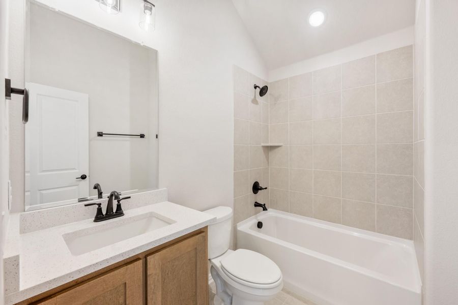 Bathroom with wood vanity, white quartz countertop, tiled tub-shower combo, and black fixtures