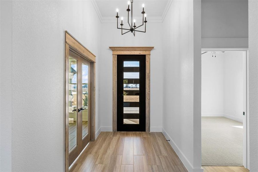 Entryway with ornamental molding, french doors, an inviting chandelier, and light wood-type flooring