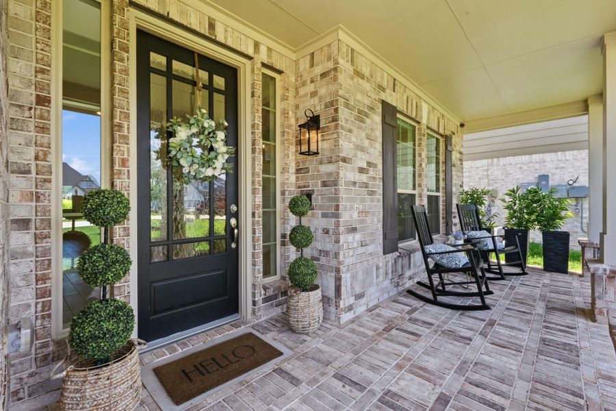 Charming and welcoming front porch. The space is adorned with potted plants and has cozy rocking chairs, perfect for relaxing.